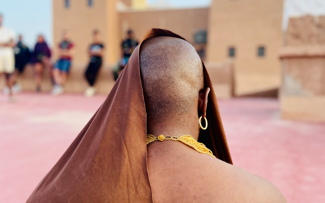 The back of a bald head partially covered with brown material, wearing a gold hoop earring and a yellow necklace