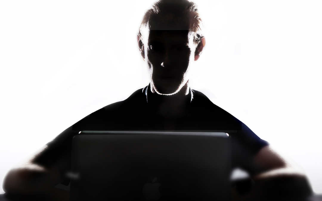Shadow of a man sat in front of a laptop on white backdrop