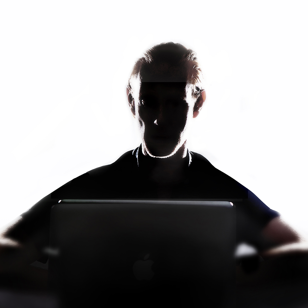Shadow of a man sat at a laptop in front of a white backdrop