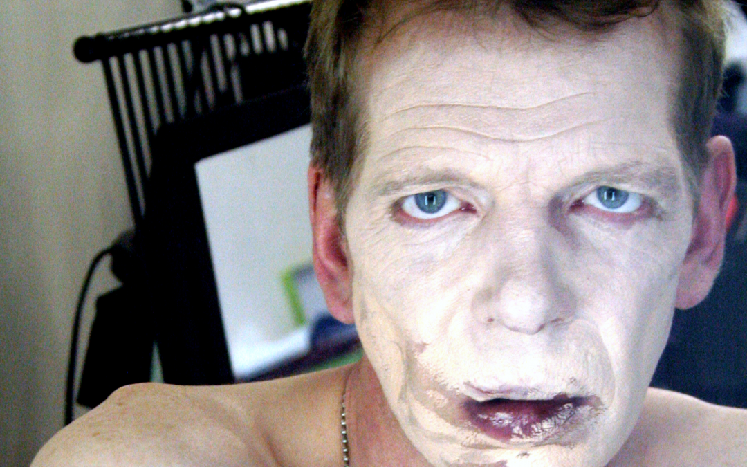 Topless man looking down the camera with smeared light makeup covering his face