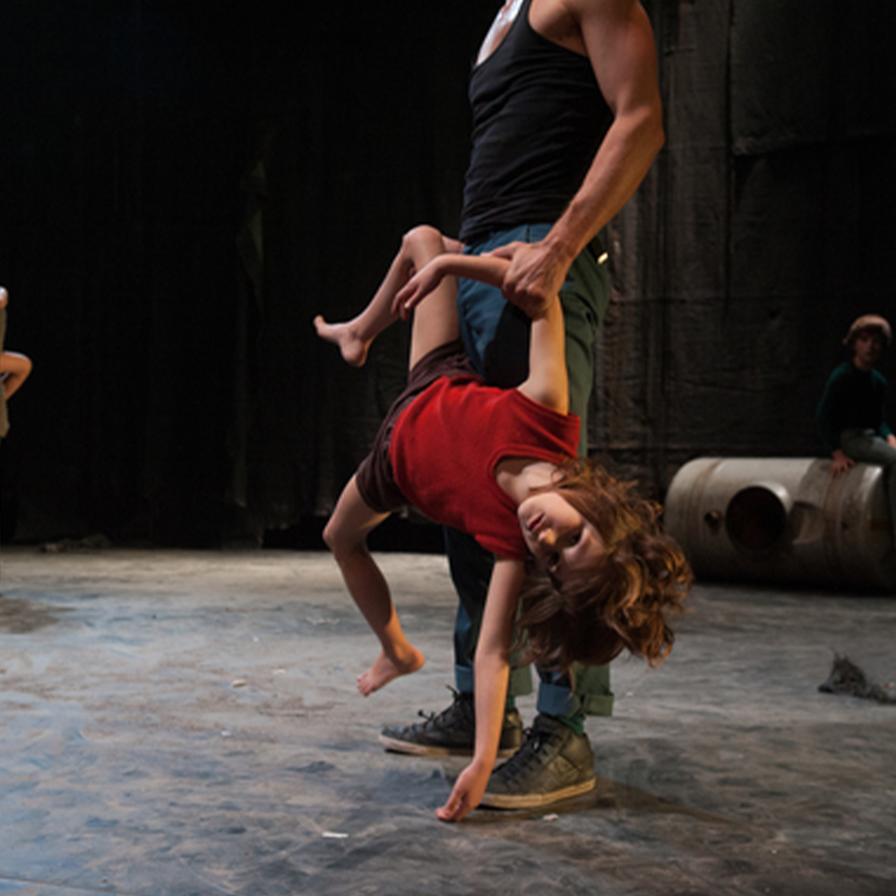 A aman in a black vest and jeans holds a young girl by an arm and a leg 