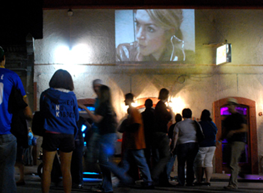 A crowd formed in the street around a projected image on a wall