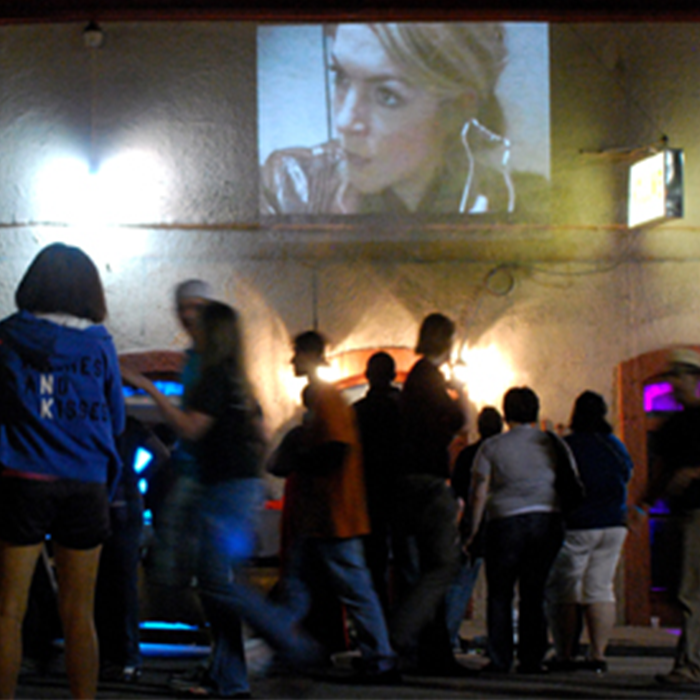 A crowd formed in the street around a projected image on a wall 