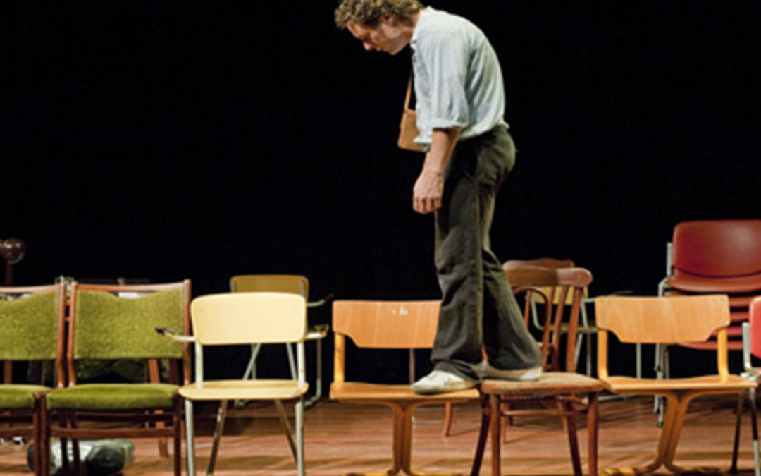 A man in shirt and trousers walking across chairs