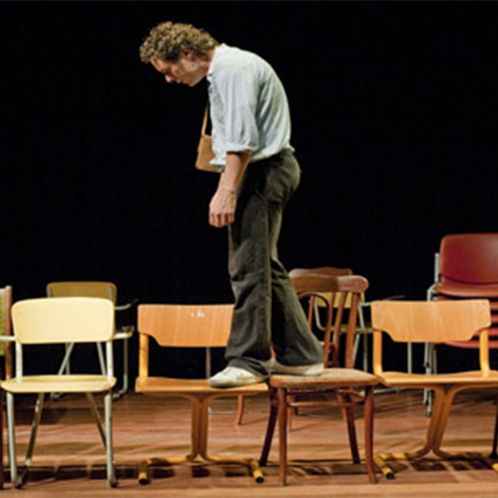 A man in shirt and trousers walking across chairs