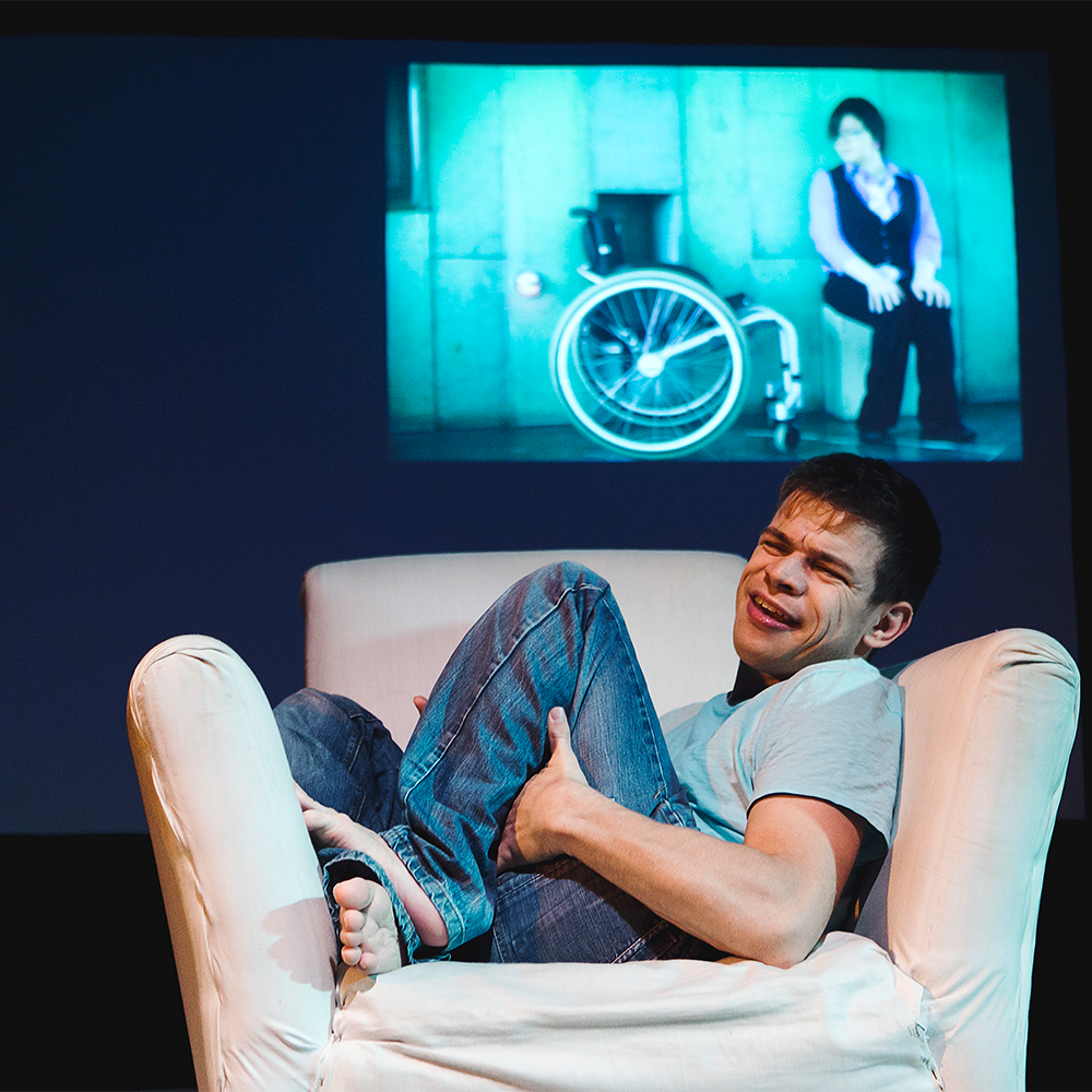 A man curled up on a white armchair in front of a blue screen