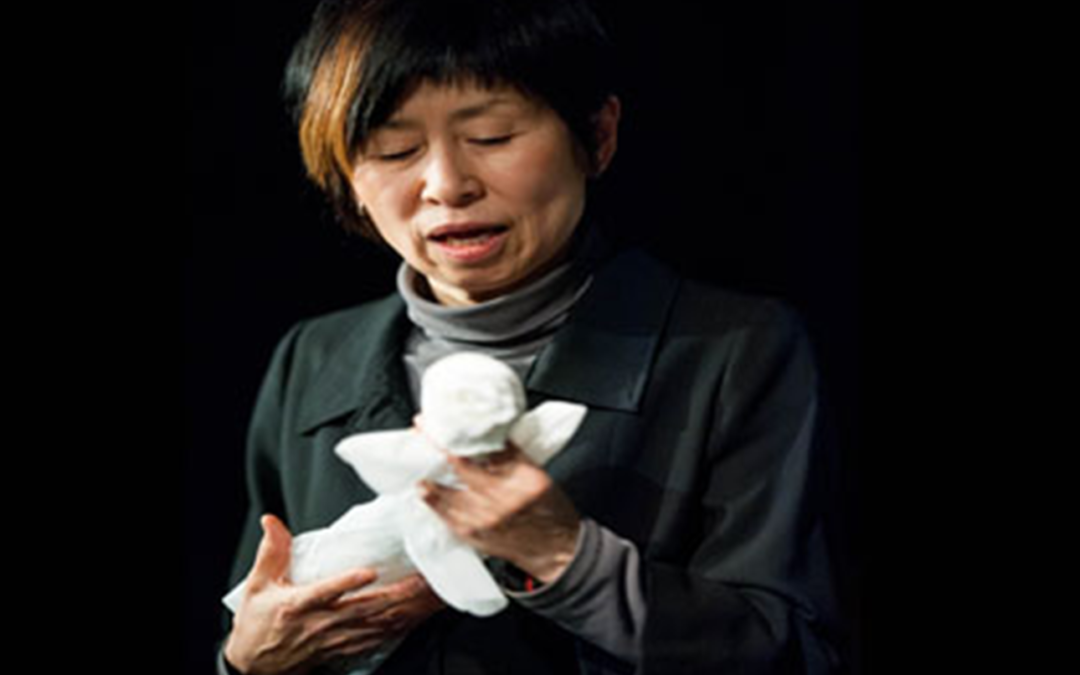 A woman in black and grey holds a white plastic bag shaped as a person