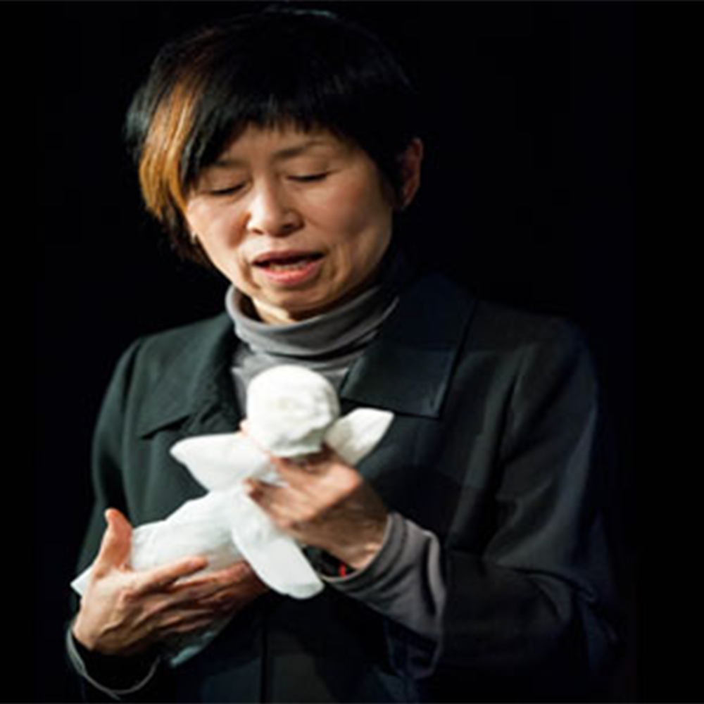 A woman in black and grey holds a white plastic bag shaped as a person