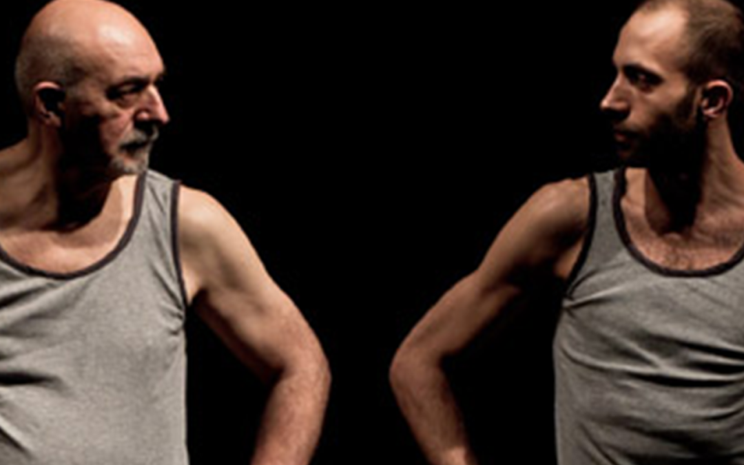 Two men in grey vests look at one another with hands on their hips