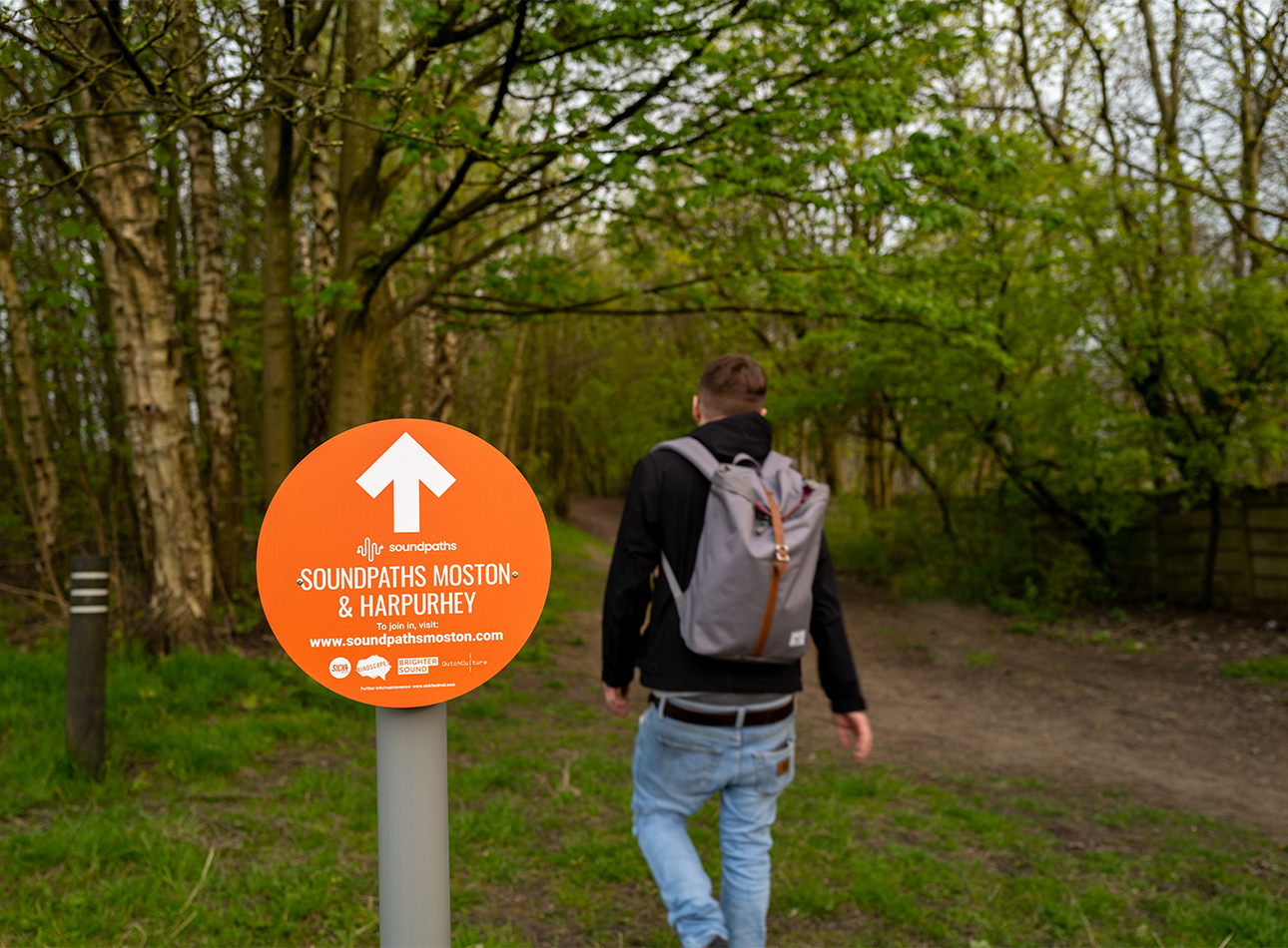 An orange sign reads 'Soundpaths' as a man is seen walking the route in nature.